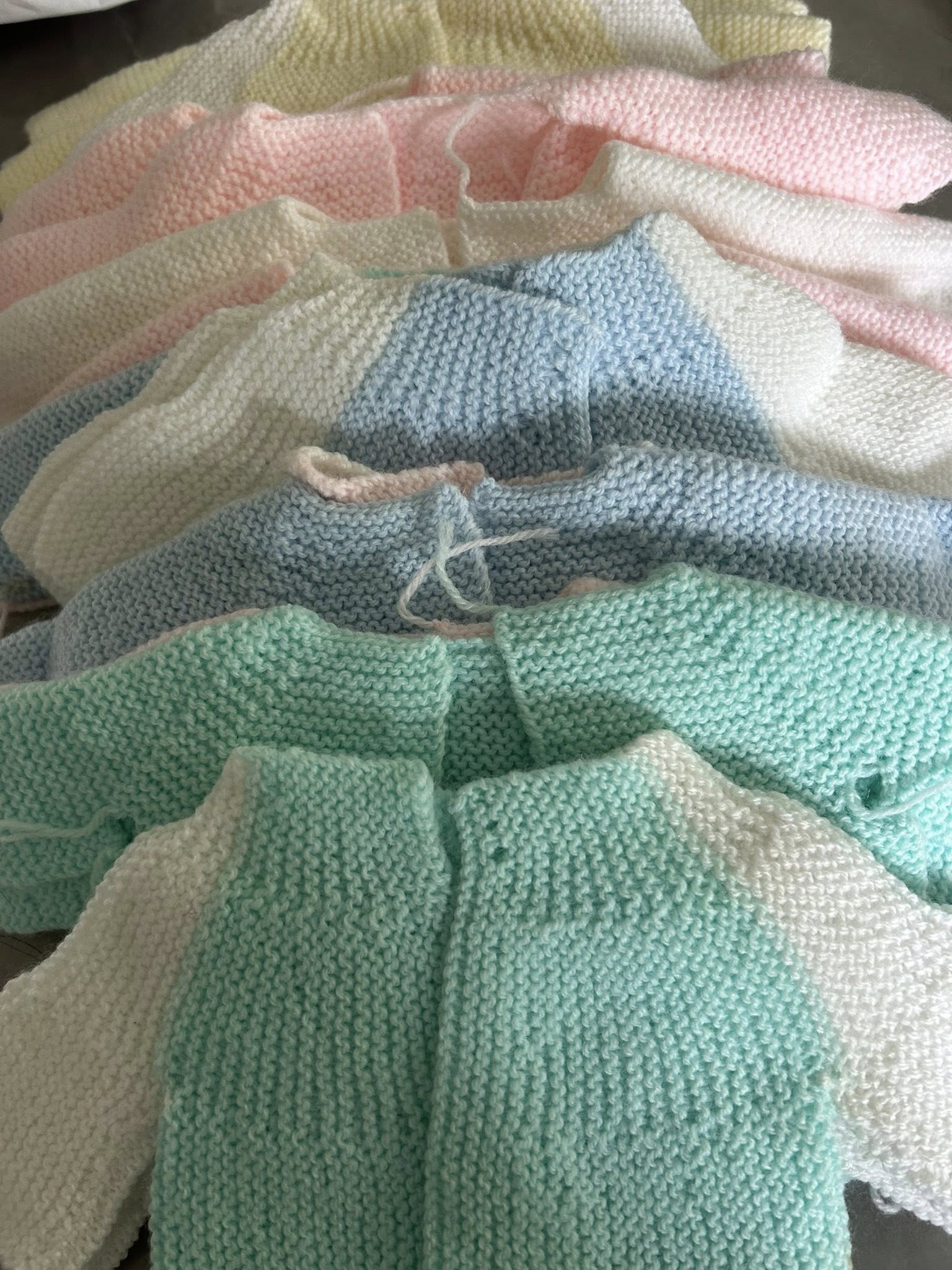 Handknitted baby clothes made by Swindon Big Knit, featuring soft yarns and a mix of tiny garments crafted by community volunteers.